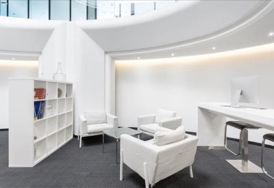 Communal lounge area with white armchairs, a glass coffee table, and shelving.