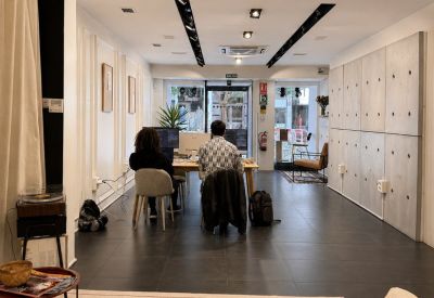 Spacious coworking area with long wooden desks, black tile flooring, and overhead track lighting.