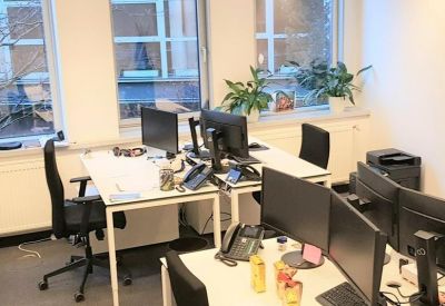 Open office area with white desks, black ergonomic chairs, and indoor plants.