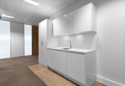 Modern office kitchen area with sleek white cabinetry and a stainless steel sink.