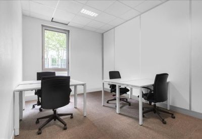 Minimalist four-person office suite with white desks and black ergonomic chairs.