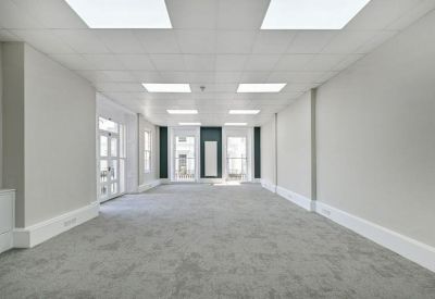 Spacious, bright open-plan office suite with grey carpeting and recessed ceiling lights.