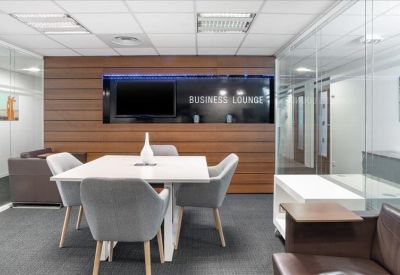 Contemporary business lounge with a wood-paneled wall, television, and plush grey seating.