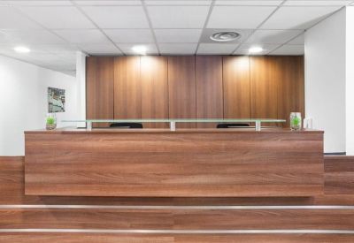 Sleek wooden reception desk in a well-lit lobby with clean white walls and ceiling lights.