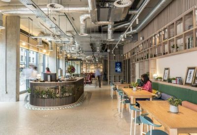 Vibrant communal lounge and cafe area with industrial ceilings and a circular wood-paneled bar.