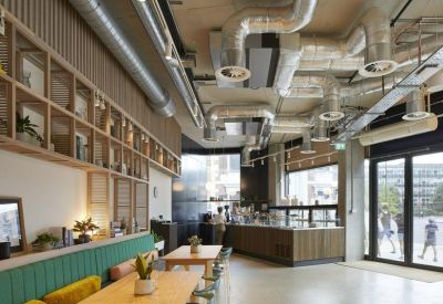 Open-plan reception and lounge area with exposed ductwork and comfortable green banquette seating.