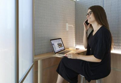Private phone booth featuring wood paneling, a laptop desk, and a woman on a call.