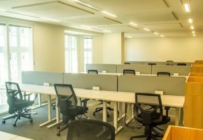 Bright open-plan workspace with rows of white desks and ergonomic mesh chairs.