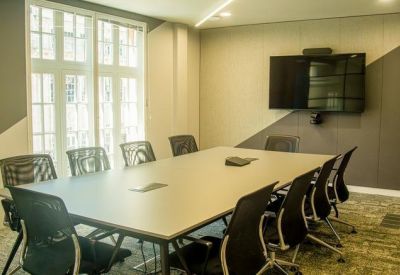 Modern meeting room with a large grey table, black chairs, and a wall-mounted TV screen.