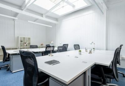 Bright open-plan workspace with white desks, ergonomic mesh chairs, and a large skylight.