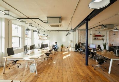 Bright coworking area with long wooden desks and black ergonomic chairs.