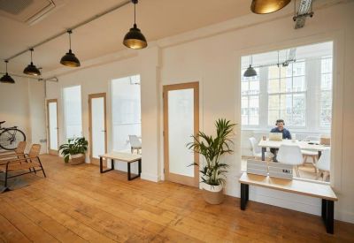 Modern hallway with several private glass-fronted office suites and a large window.
