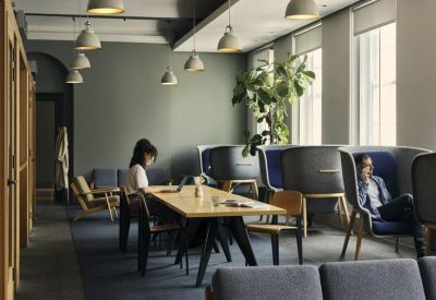Coworking lounge with a long wooden table, blue privacy booths, and hanging pendant lights.