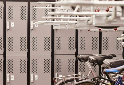 Secure indoor bicycle storage room with tiered metal racks and grey lockers.