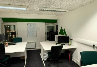 Bright office space with two white corner desks, black rolling chairs, and a wall-mounted whiteboard.