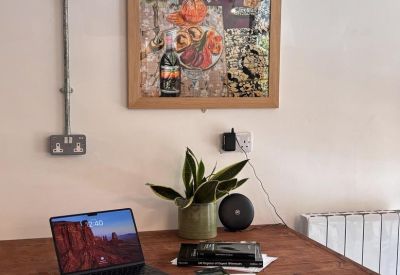 Wooden workstation with a laptop, plant, and colorful framed artwork on the wall.