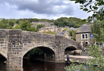 Scenic exterior view of a stone arch bridge over a river with hills in the background.