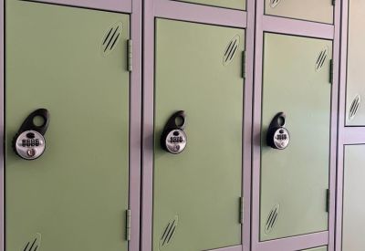 Bank of green storage lockers with combination locks in a bright room.