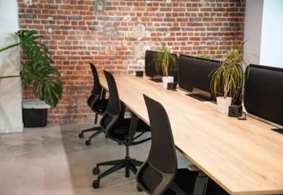 Long wooden shared workstation with ergonomic chairs against an exposed brick wall.
