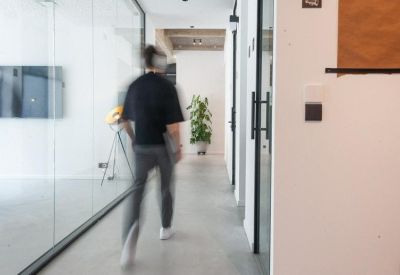 Bright white hallway with glass-walled offices and a green plant at the end.