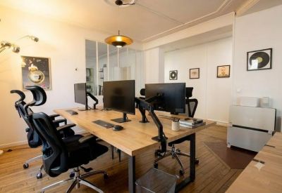 Shared office space with light wood desks and ergonomic black chairs.