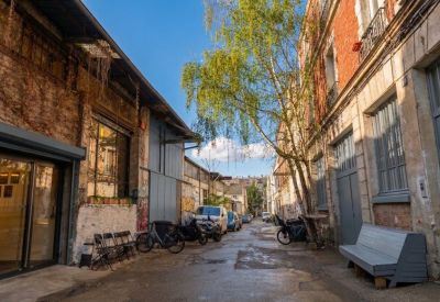 A narrow paved courtyard lined with historic industrial buildings and trees.