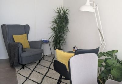 Cozy lounge area with a grey wingback chair, yellow pillow, and patterned rug.