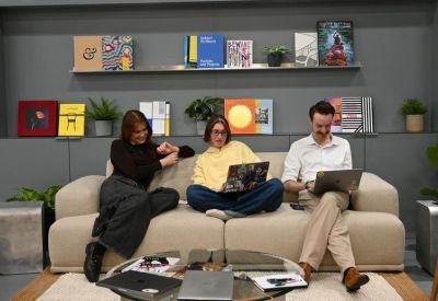 Three people working on laptops while seated on a comfortable beige sofa.