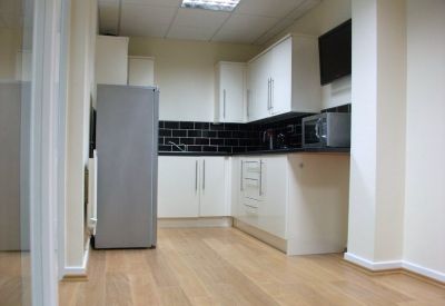 Modern communal kitchen with white cabinetry, dark tiling, and wood-effect flooring.