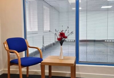 Reception waiting area with a blue armchair and a small wooden side table.