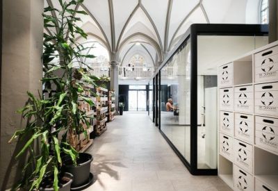 Interior walkway flanked by glass partitions, indoor plants, and a wall of white storage cubbies.