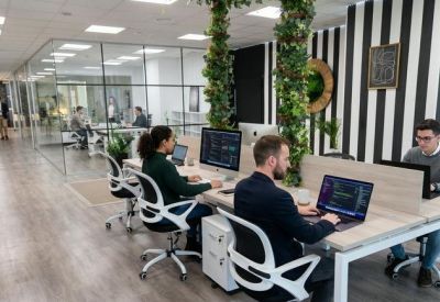Modern workstation in a glass-partitioned office with hanging plants and striped wall decor.