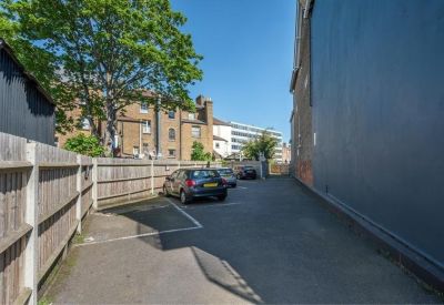 Private paved parking area adjacent to a grey building wall and wooden fence.