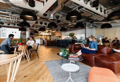 Lively coworking lounge with industrial ceilings, leather seating, and people working.