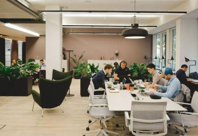 Spacious coworking area with people working at long white tables and potted plants.