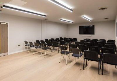 Spacious seminar room with rows of black chairs facing a wall-mounted screen.