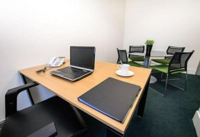 Private office suite with a laptop on a wooden desk and a small meeting table in the background.