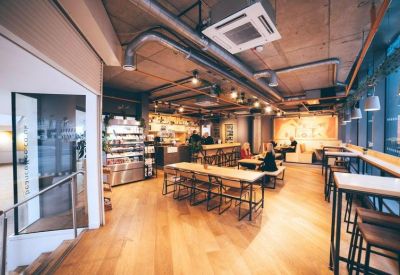 Spacious communal cafe with long wooden tables and exposed industrial ceilings.