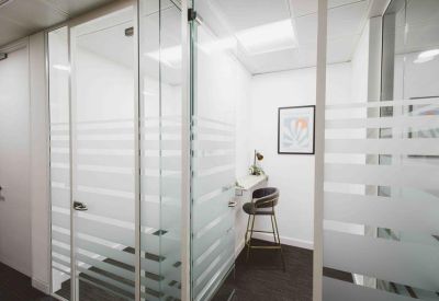 Private glass-walled phone booth or focus room with a single high stool.