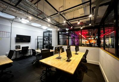 Minimalist coworking area with long wooden tables and black office chairs.