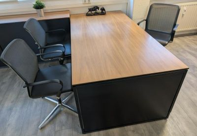 Modern wooden desk with black mesh chairs in a bright office environment.