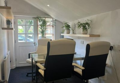 Bright meeting room under a sloped ceiling with a glass table, white chairs, and potted plants.