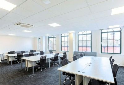 Spacious office room with rows of white desks and black ergonomic chairs near large windows.