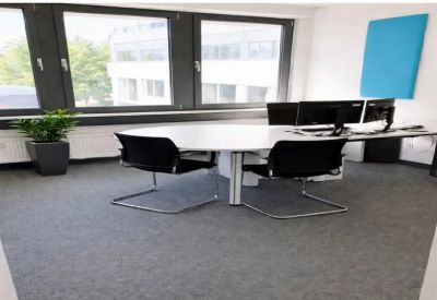 Oval conference table in a sunlit meeting room with dual monitors and a vibrant blue wall panel.