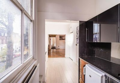 Bright hallway leading from a modern kitchen into a spacious wooden-floored room.