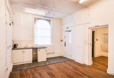 Compact kitchenette area with white base units and large sash window.