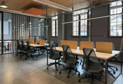 Open-plan workspace with wooden desks, mesh chairs, and industrial ceiling details.