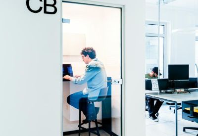 Glass-walled private phone booth with a person working on a laptop.