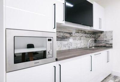 Modern white office kitchen with integrated microwave and grey wood-effect countertop.
