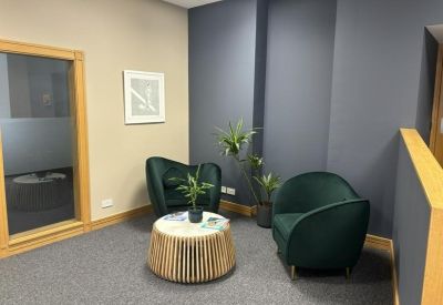 Lounge area featuring deep green velvet armchairs and a slatted wood coffee table.